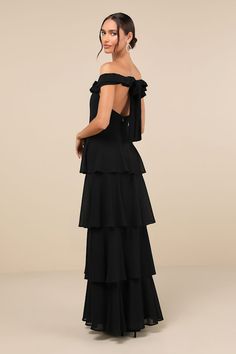 the back of a woman wearing a black dress with tiered layers and open shoulders