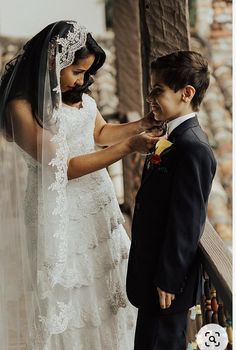 a woman in a wedding dress is helping a young boy put on his boutonniere