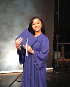 a woman in a purple graduation gown is holding up a blue piece of paper and posing for the camera