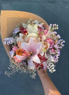 a bouquet of flowers is being held by someone's hand in front of the water