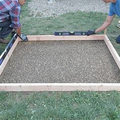 two men working on building a raised garden bed in the yard with tools and gravel