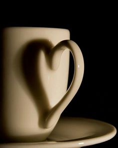 a white coffee cup with a heart shaped saucer on the side, in front of a black background