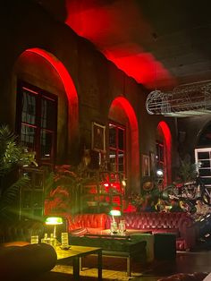 a dimly lit room with red lighting and couches in the center, surrounded by potted plants