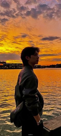 a man standing on top of a wooden pier next to the ocean under a colorful sky