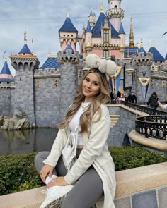 a beautiful woman sitting on top of a stone wall next to a castle with turrets