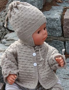 a baby doll sitting on top of a pile of rocks wearing a knitted sweater and hat