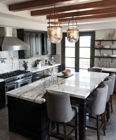 an image of a kitchen with marble counter tops and black cabinets, along with two chandeliers hanging from the ceiling