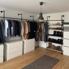 an organized closet with clothes and shoes hanging on the wall, along with white drawers