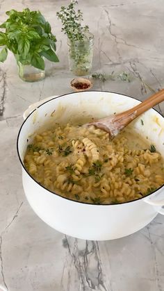 a pot filled with pasta and parsley on top of a table next to a wooden spoon