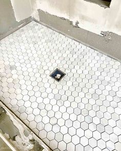 a bathroom floor with a hole in the middle and white tiles on the wall behind it