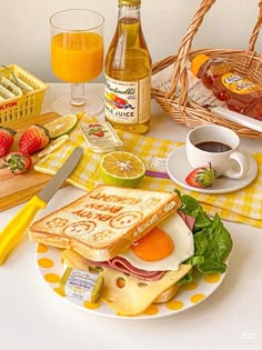 a table topped with sandwiches and fruit next to bottles of orange juice on top of a white table