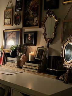 a desk with books, candles and pictures on the wall next to it in front of a mirror