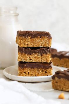 three pieces of chocolate peanut butter bars stacked on top of each other next to a bottle of milk