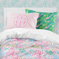 a bed with pink and green floral comforter, two pillows and a monogrammed pillow