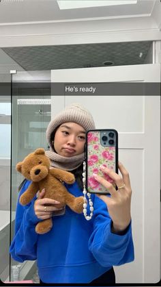 a woman is holding a teddy bear and taking a selfie with her cell phone