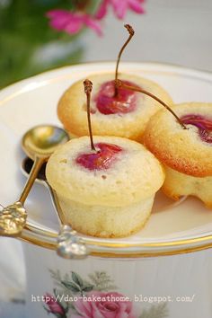 three small pastries on a plate with spoons and flowers in the back ground