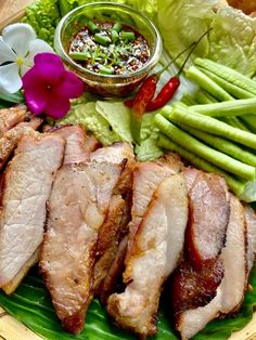 sliced pork on a plate with green beans, asparagus and flower next to it