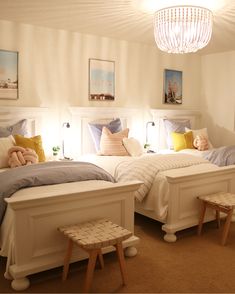 two twin beds in a bedroom with white walls and carpeted flooring, one has a chandelier above the bed