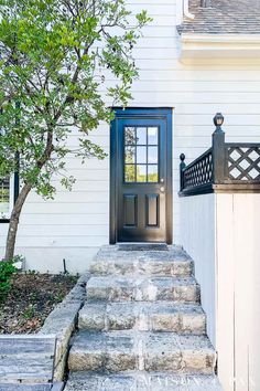 a black door is on the side of a white house with steps leading up to it