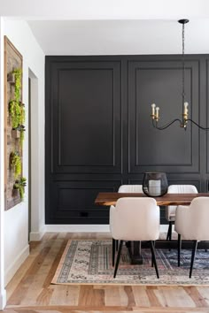 an elegant dining room with black walls and white chairs, wooden table and chandelier