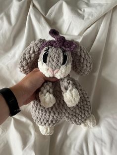 a hand holding a crocheted stuffed animal on top of a white bed sheet