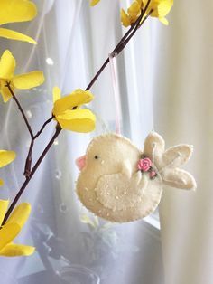 a stuffed bird hanging from a twig with yellow flowers in the background and a white curtain behind it