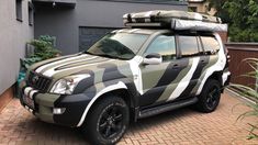 an suv with a surfboard on top parked in front of a house and bushes