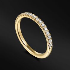 a yellow gold wedding band with rows of diamonds on the side, in front of a black background