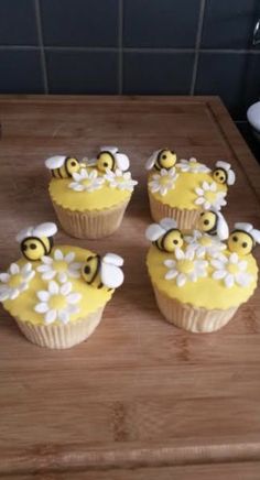 four cupcakes with yellow frosting and white flowers on them sitting on a cutting board