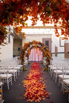 an outdoor ceremony with white chairs and red petals on the aisle, surrounded by fall leaves