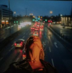 a woman looking up at traffic on a busy city street in the evening with her eyes closed