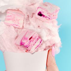 a hand holding a cup filled with marshmallows and pink frosted squares