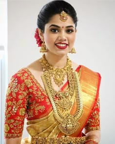 a woman in a red and gold sari with jewelry on her neck, smiling at the camera