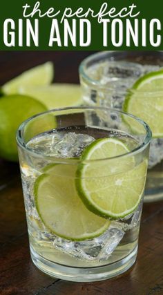 two glasses filled with gin and tonic sitting on top of a wooden table next to limes