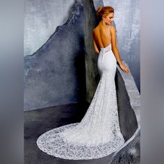 a woman in a white wedding dress leaning against a wall with her back to the camera