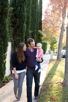 a man, woman and child walking down the sidewalk in front of some tall trees