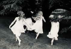 three girls in white dresses are running through the grass