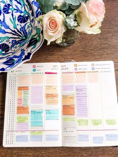 an open planner sitting on top of a wooden table next to a vase with flowers