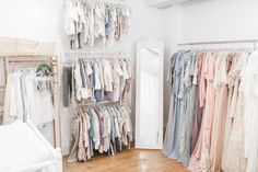 a room filled with lots of clothes on hangers next to a white dresser and mirror