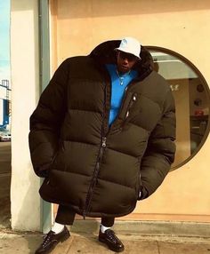 a man in a puffy coat and hat standing on the sidewalk