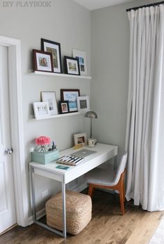 a white desk sitting under a window next to a chair and pictures on the wall