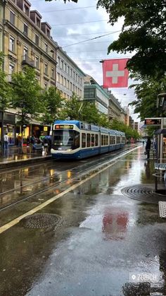 a blue and white train traveling down tracks next to tall buildings on a rainy day