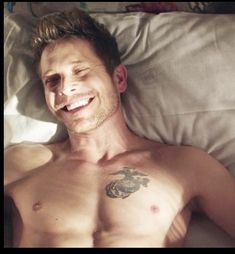 a shirtless man laying in bed with his eyes closed and tattoos on his chest