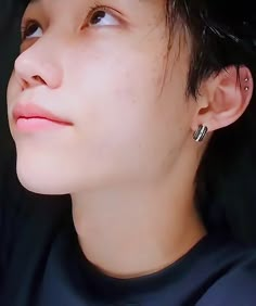 a close up of a person with black hair and piercings on their ears looking off into the distance