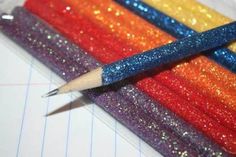 a pencil is sitting on top of some glittered paper and it's in the shape of a rainbow