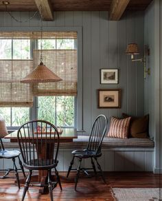 a table and chairs in a room with wood flooring, two windows and wooden blinds