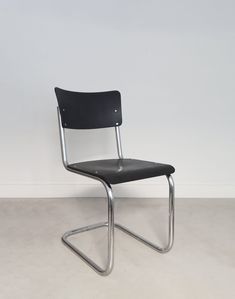 a black chair sitting on top of a floor next to a white wall with a metal frame