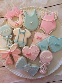 a plate full of decorated baby cookies on a wooden table with pink, blue and white ones