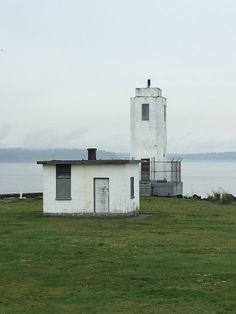 a small white building sitting on top of a lush green field next to the ocean