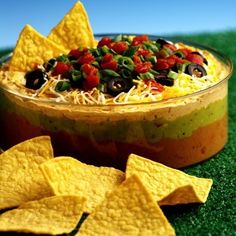 a bowl filled with salsa and tortilla chips on top of green carpeted grass